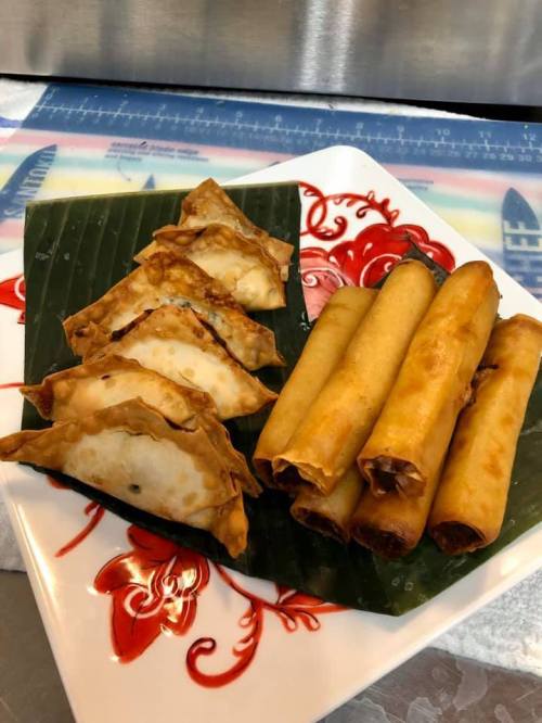 A plate with crispy dumplings and spring rolls, garnished with banana leaves and a decorative red pattern.