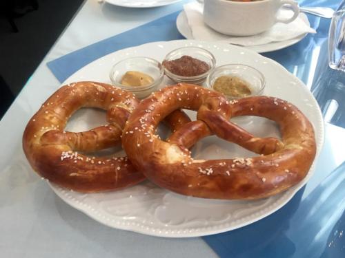Two large, soft pretzels on a white plate, served with three small bowls of mustard and dipping sauces.
