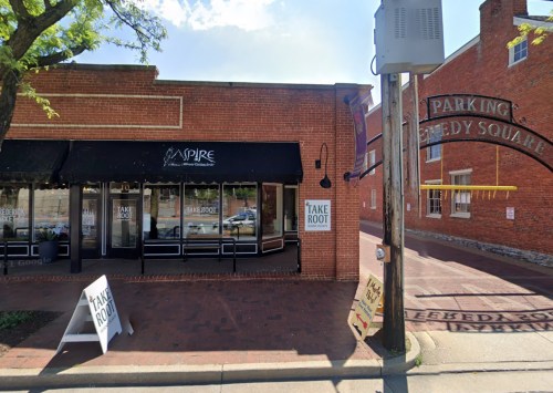 A brick building with large windows displaying "Take Root" and "Aspire" signs, located at a street corner.