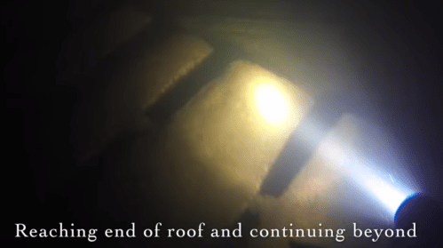 A flashlight illuminates a dark area, revealing the end of a roof and a continuation beyond it.