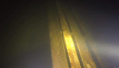 Underwater view of a submerged structure with rusted metal beams illuminated by soft light.