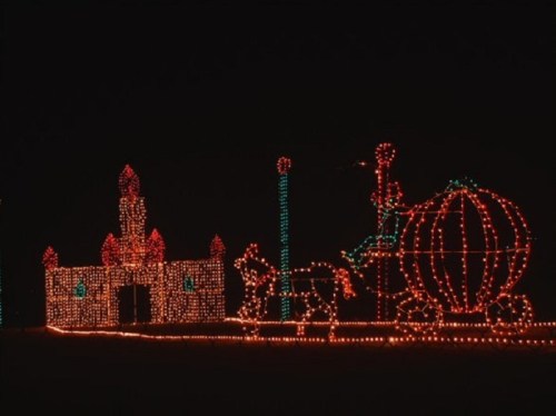 Colorful holiday lights form a castle and a carriage, creating a festive scene against a dark night sky.