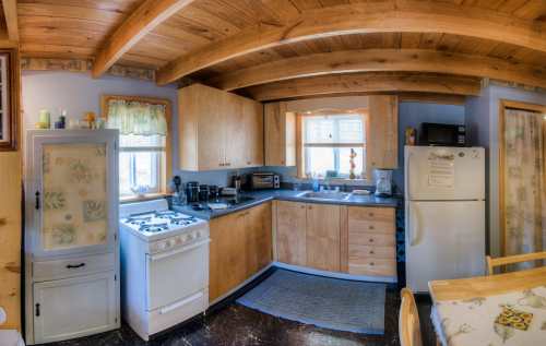 Cozy kitchen with wooden beams, light wood cabinets, a stove, refrigerator, and a small dining table.