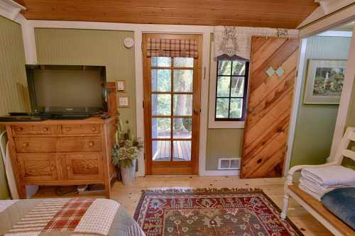 Cozy interior of a room featuring a wooden dresser, TV, and doors leading to a deck with greenery outside.