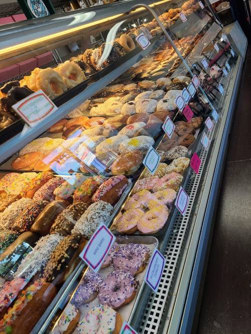 A display case filled with a variety of colorful donuts, including glazed, frosted, and sprinkled options.