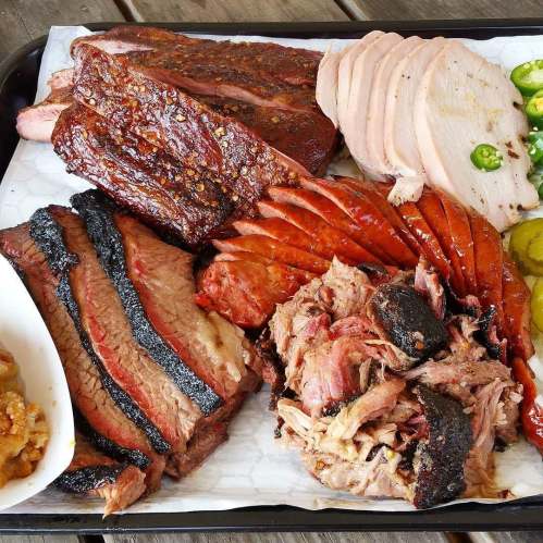 A platter of assorted smoked meats including brisket, turkey, sausage, and pulled pork, garnished with pickles and jalapeños.