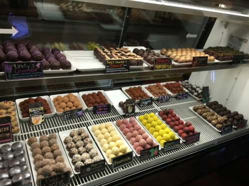 A display case filled with various colorful chocolate truffles and confections, labeled with names and flavors.