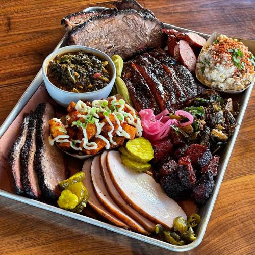 A platter of assorted barbecue meats, including brisket, sausage, and turkey, with sides of pickles, greens, and rice.