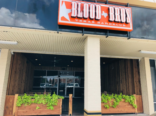 Exterior of Blood Bros. Texas Barbecue, featuring a wooden facade and planters with greenery.