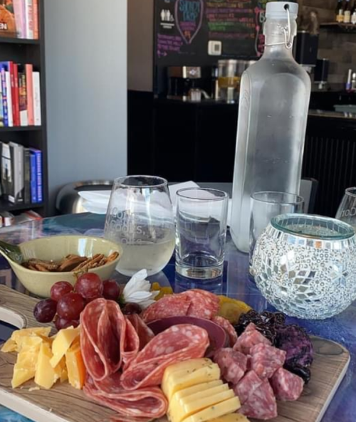 A charcuterie board with meats, cheeses, grapes, and a glass of white wine, set on a table with decorative items.