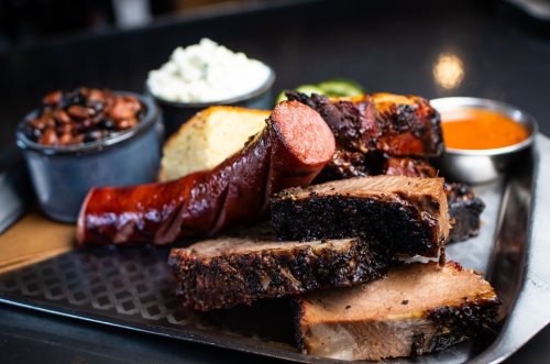 A platter of smoked meats including brisket and sausage, served with sides of beans, coleslaw, and bread.