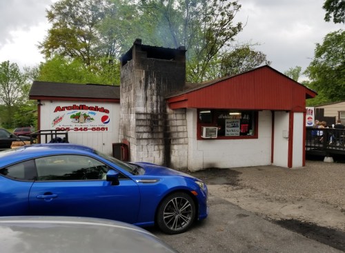 A blue car parked in front of a small restaurant with a chimney emitting smoke and a sign for Archibald's.