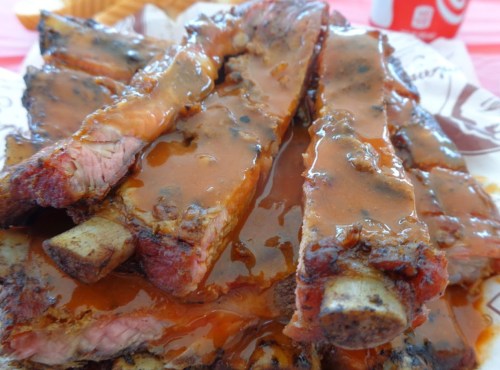 A close-up of juicy, sauced ribs stacked on a plate, showcasing a rich, glossy barbecue sauce.