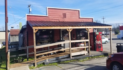 A small red building with a wooden porch, featuring a Coca-Cola vending machine outside.
