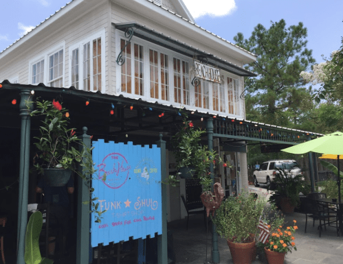 A colorful restaurant exterior with a sign reading "The Backyard," surrounded by greenery and festive lights.