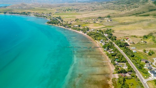 Aerial view of a serene lake shoreline with clear blue water, green hills, and scattered houses along the coast.