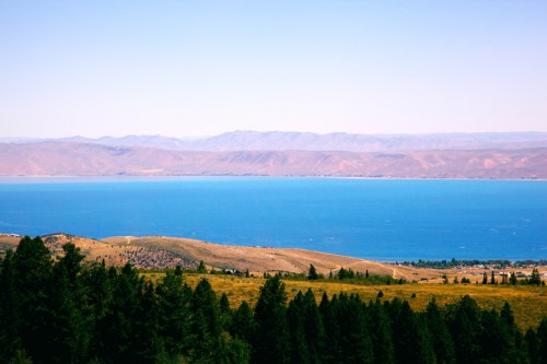 A serene landscape featuring a blue lake surrounded by mountains and lush green trees under a clear sky.