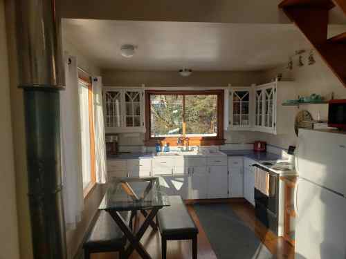 Bright kitchen with white cabinets, a dining table, and large windows overlooking trees. Cozy and inviting atmosphere.