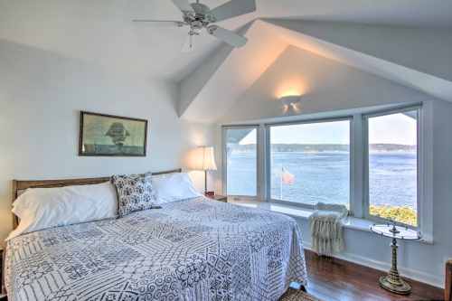 Bright bedroom with a large window overlooking the water, featuring a bed, lamp, and decorative artwork.