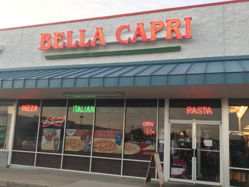 Exterior of Bella Capri restaurant with neon signs for pizza and pasta, featuring a casual dining atmosphere.