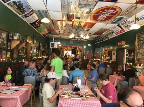 A bustling restaurant filled with diners at checkered tables, decorated with vintage signs and warm lighting.