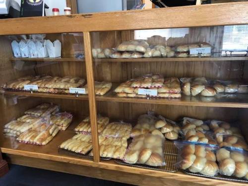 A display case filled with various types of baked goods, including rolls and pastries, neatly arranged on shelves.