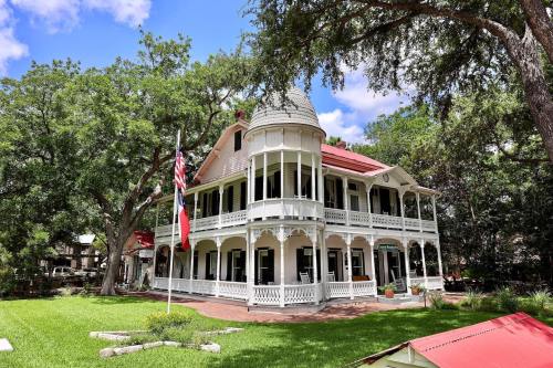 A charming two-story Victorian-style house with a turret, surrounded by trees and a green lawn.