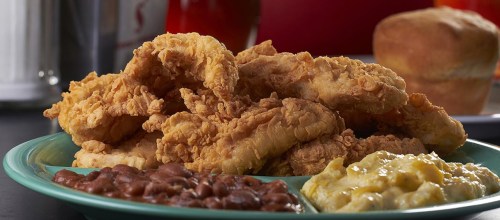 A plate of crispy fried chicken strips with sides of baked beans and creamy macaroni and cheese, plus a biscuit.