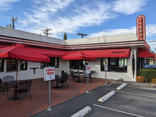 Exterior of Bubba's restaurant featuring red umbrellas, outdoor seating, and signs for curbside parking.