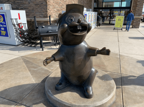 A cheerful bronze statue of a cartoonish character with a hat, standing outside a store.