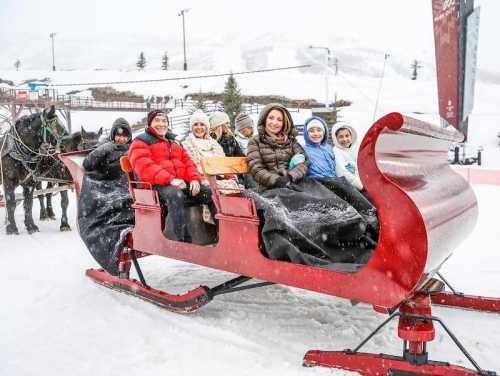 A group of people in winter clothing sitting in a red sleigh, surrounded by snow and a snowy landscape.