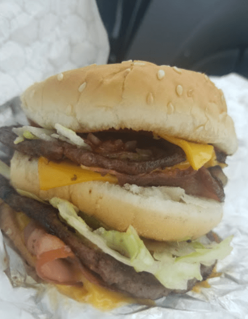 A close-up of a stacked hamburger with lettuce, cheese, and multiple layers of beef, served in a sesame seed bun.
