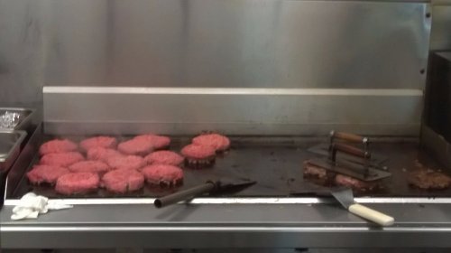 Grilling burgers on a flat top, with raw patties and cooking tools visible in a kitchen setting.