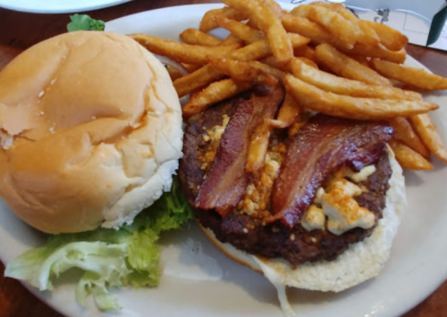 A burger with bacon and cheese on a bun, served with a side of crispy French fries and lettuce.