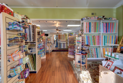 A colorful fabric store interior with shelves of patterned fabrics and a warm wooden floor.
