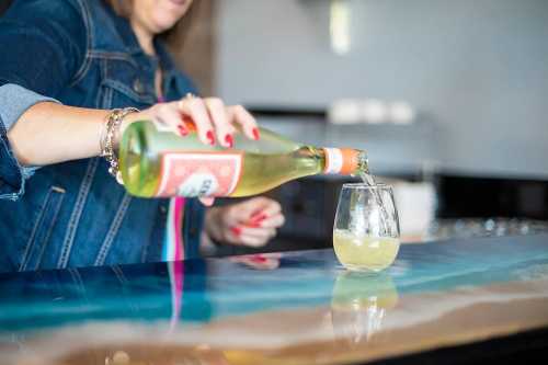 A person pours a drink from a bottle into a glass on a colorful countertop.