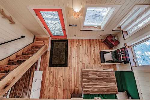 A cozy interior of a small house featuring wooden floors, a green sofa, a table, and a bright orange door.