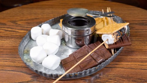 A metal tray with marshmallows, chocolate bars, graham crackers, and a s'mores maker with skewers.