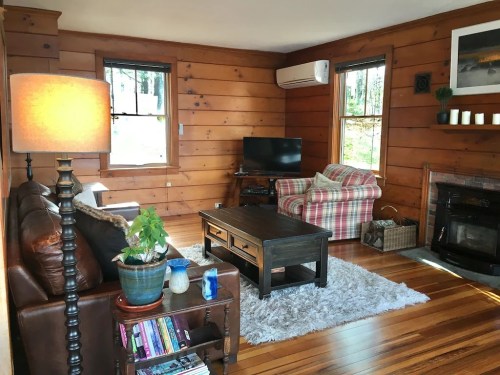 Cozy living room with wooden walls, a sofa, plaid chair, coffee table, TV, and a warm ambiance.