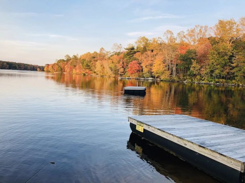 A serene lake scene with colorful autumn trees reflecting on the water, featuring a small dock in the foreground.