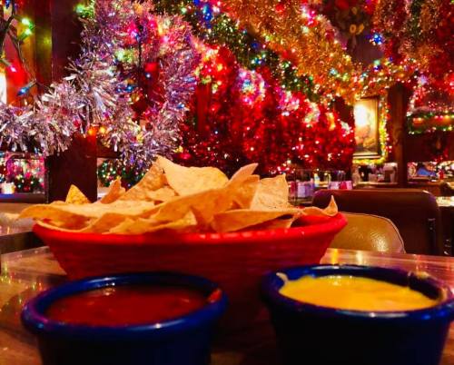 A basket of tortilla chips with salsa and cheese dip, surrounded by colorful holiday lights and festive decorations.