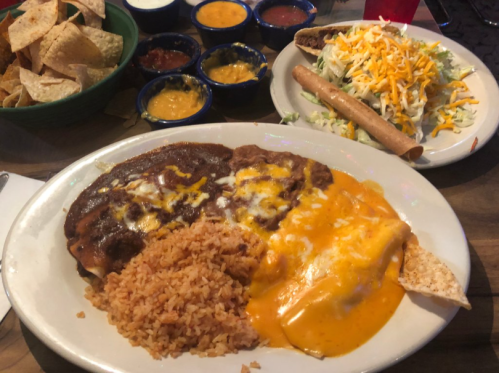 A plate of Mexican food featuring rice, beans, cheese enchiladas, and a side of salad, with tortilla chips in the background.