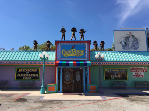 Colorful restaurant exterior with a sign reading "Campo Verde," featuring statues on the roof and a "Help Wanted" sign.