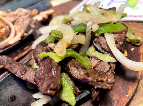 Sizzling beef fajitas with green and yellow peppers, and onions on a hot skillet.
