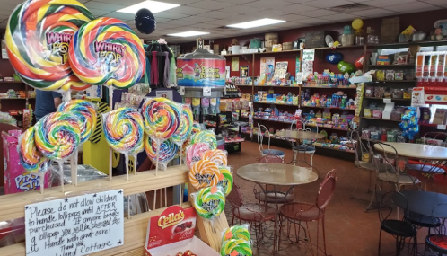 A colorful candy shop interior with shelves of sweets, lollipops in the foreground, and tables for customers.