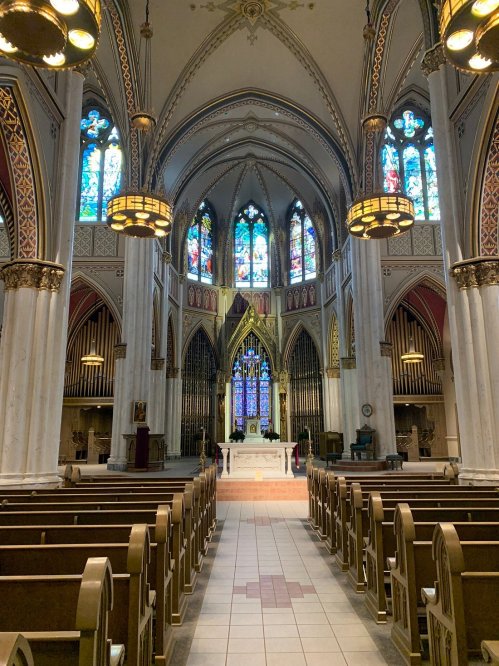 Interior of a grand church featuring stained glass windows, ornate architecture, and wooden pews.