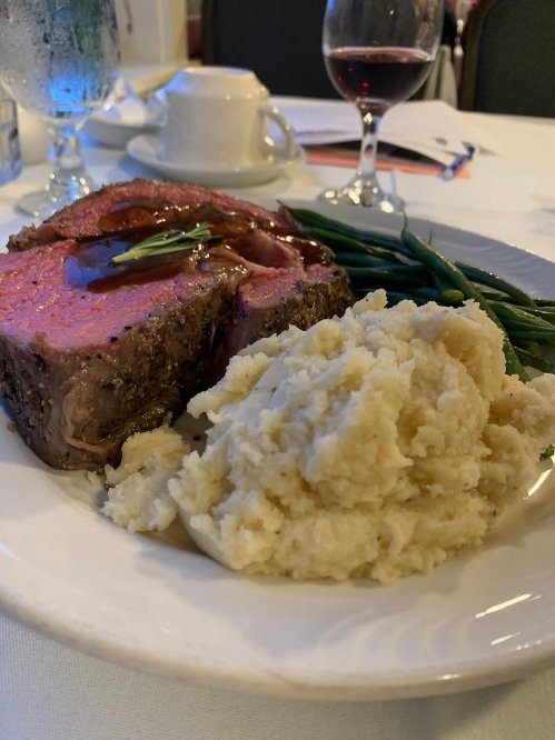 A plate featuring sliced roast beef with gravy, mashed potatoes, and green beans, set on a dining table.