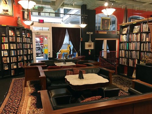 Cozy library interior with dark wood shelves, plush seating, and a decorative rug, featuring books and artwork.