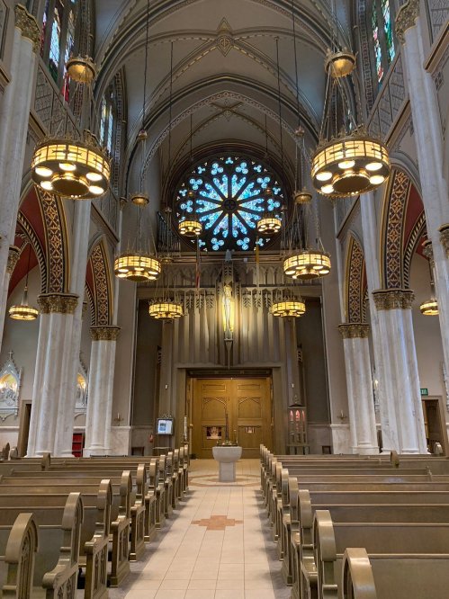 Interior of a church featuring tall arches, stained glass windows, and wooden pews leading to a central altar.