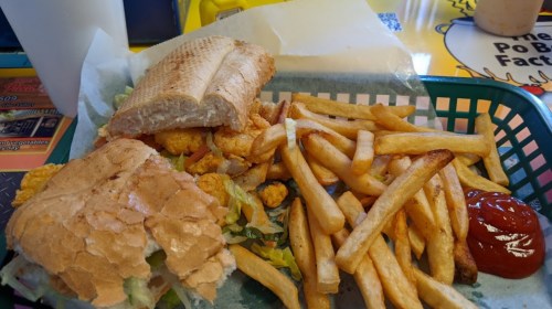 A sandwich with shrimp and lettuce, served with fries and ketchup in a green basket on a colorful table.
